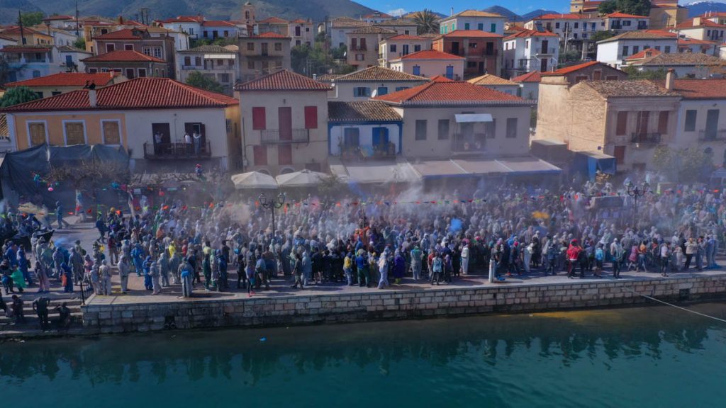 Aerial drone bird's eye view photo of people participating in traditional colourful flour war or Alevromoutzouromata part of Carnival festivities in historic port of Galaxidi, Fokida, Greece